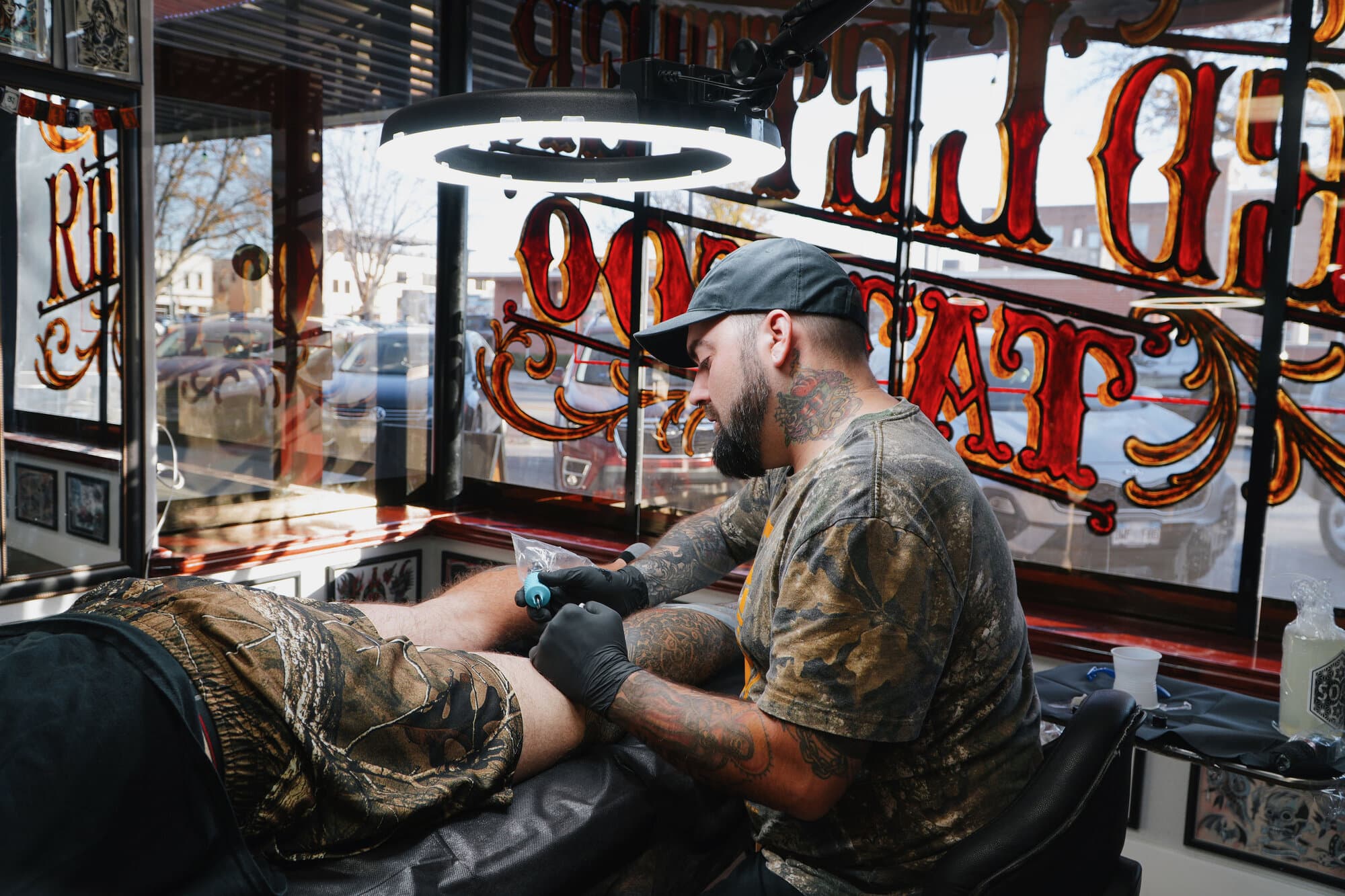 Mike Horman tattooing a client at his station behind the shop's hand-painted window