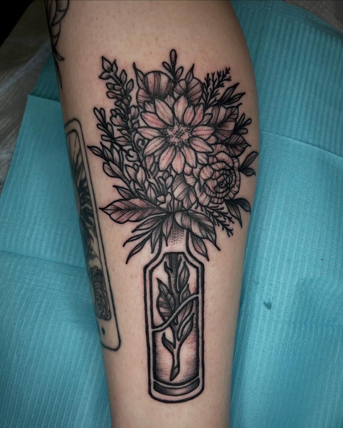 Black and gray floral bouquet in a vase leg tattoo